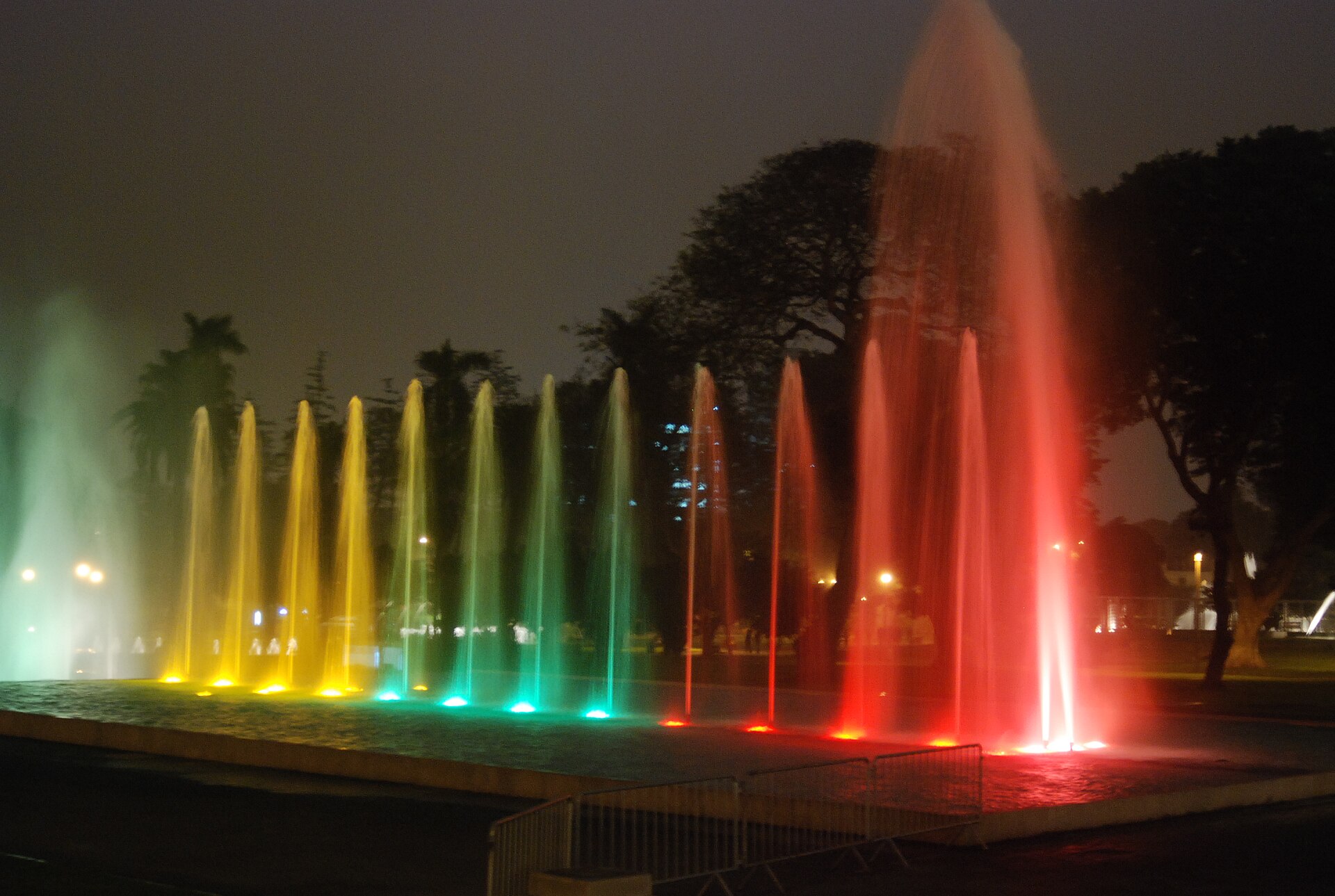 A row of illuminated fountains glowing yellow, green and red at night at the Circuito Mágico del Agua in Lima