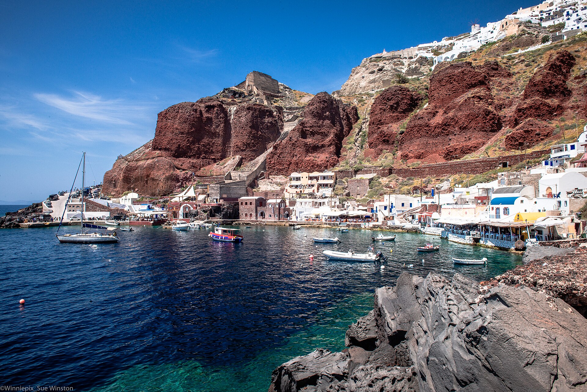 Ammoudi Bay below Oia, with red cliffs, fishing boats and waterside tavernas